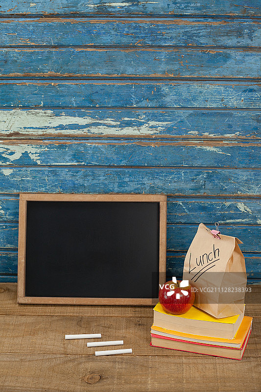 蓝色木质背景上的石板、粉笔、苹果、午餐包和书籍图片素材