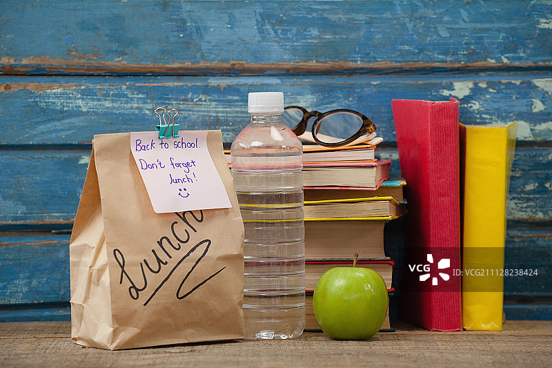 蓝色木质背景上的书堆、苹果、水瓶、眼镜和午餐包图片素材