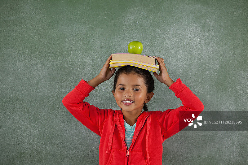 年轻女孩头顶着书和苹果的肖像图片素材