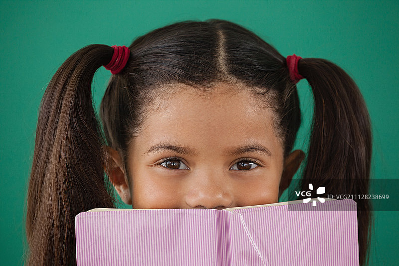 躲在书后的女学童肖像，背景为绿色图片素材