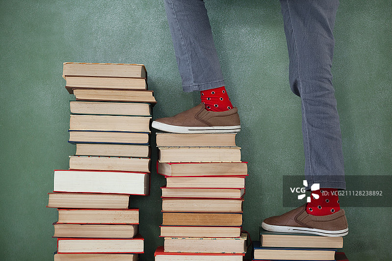 小学生爬上书堆台阶，背景是黑板的下半身图片素材