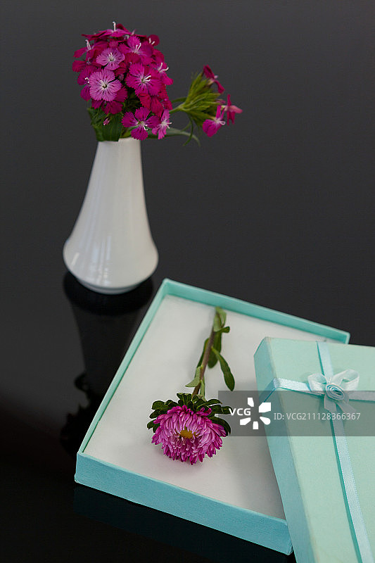 黑色背景上带有鲜花和花瓶的已打开礼品盒图片素材