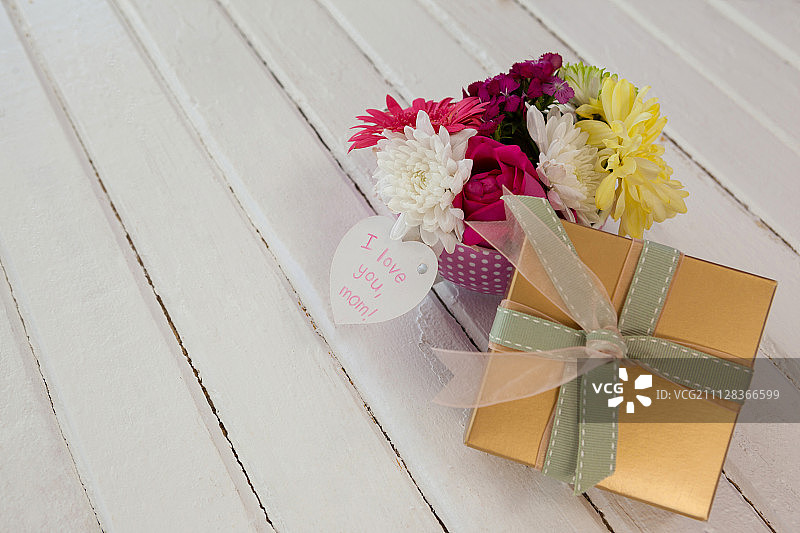 木质表面上的礼品盒与鲜花，附带“我爱你妈妈”贺卡图片素材