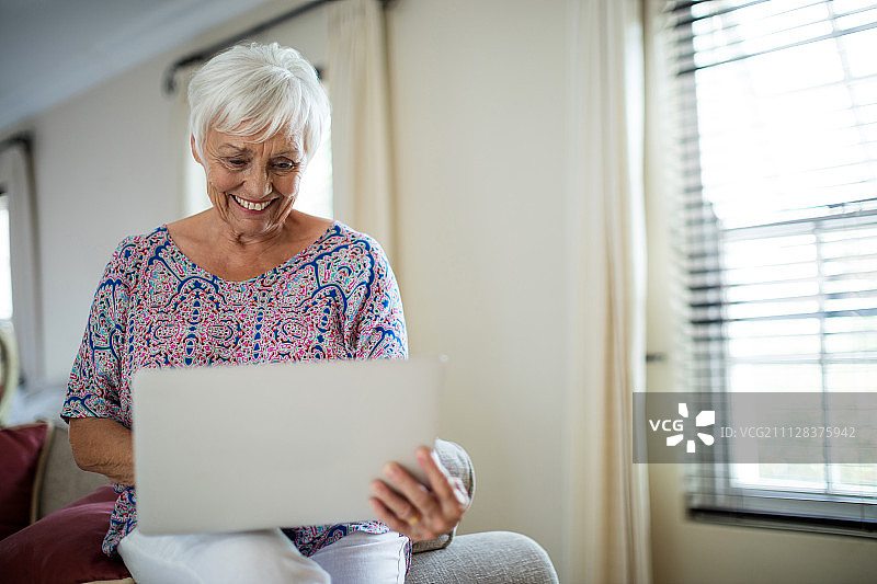 年长的女人在家中客厅使用笔记本电脑图片素材