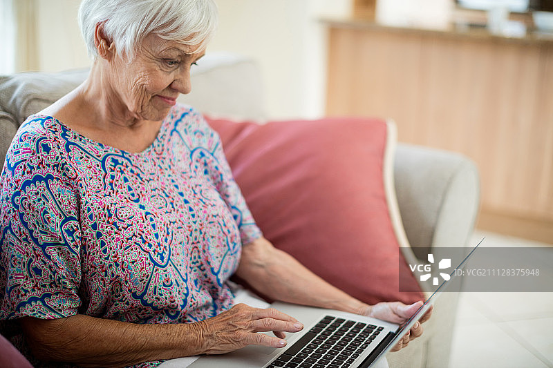年长的女人在家中客厅使用笔记本电脑图片素材