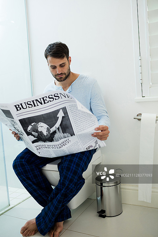 男人坐在家里的马桶上读报纸图片素材