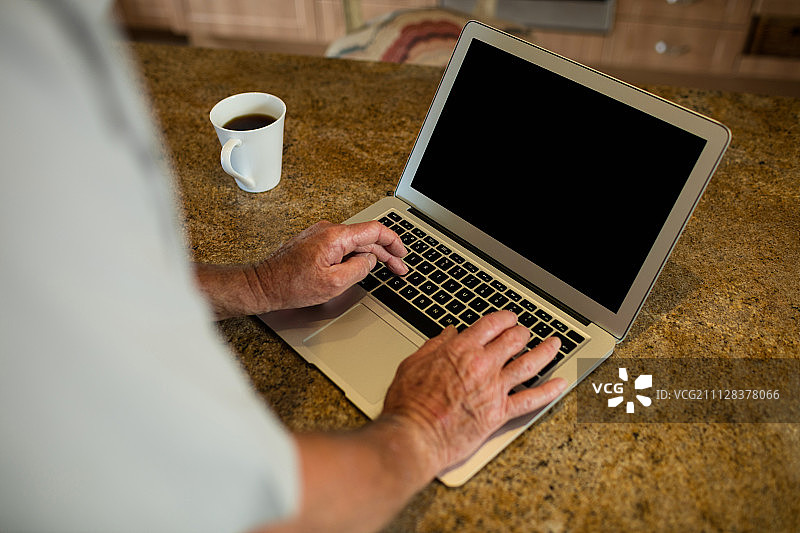 在家中厨房使用笔记本电脑的年长男人身体中部图片素材