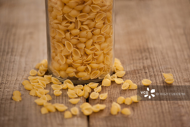 贝壳形意大利面从玻璃罐中洒在木质背景上图片素材
