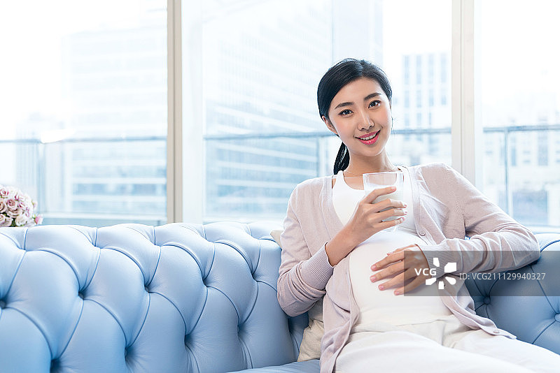 年轻孕妇在沙发上喝牛奶图片素材