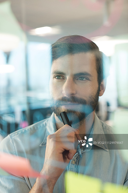 在办公室里看着写在玻璃上的计划的沉思的商人图片素材