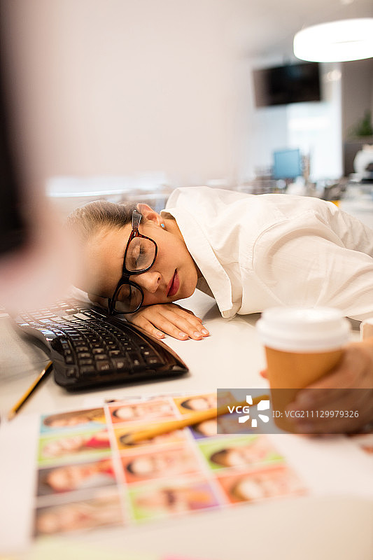 俯视视角：疲惫的女商人在创意办公室的桌子上小憩图片素材