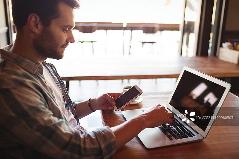 男人在餐厅使用笔记本电脑时手持手机图片素材