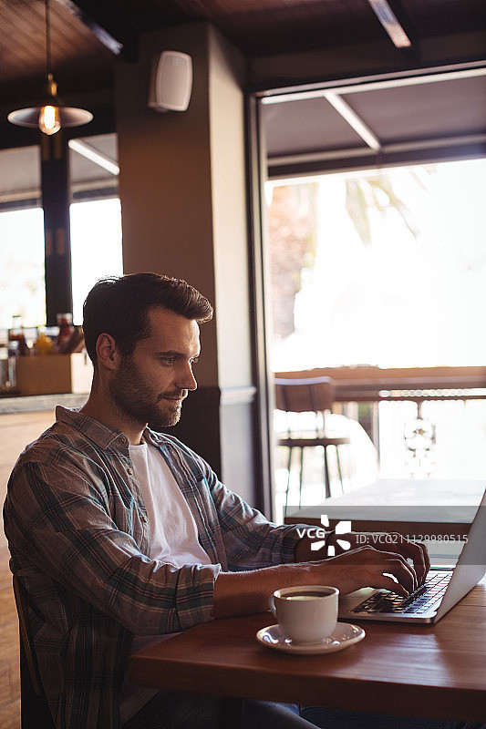 在餐厅喝咖啡时使用笔记本电脑的男人图片素材