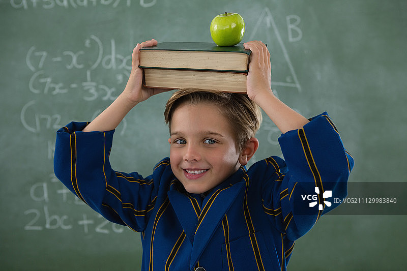 学童抱着书本，头顶苹果站在黑板前的人物肖像图片素材