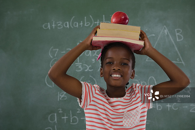 女学生手捧书本，头顶苹果，背景为黑板的肖像图片素材