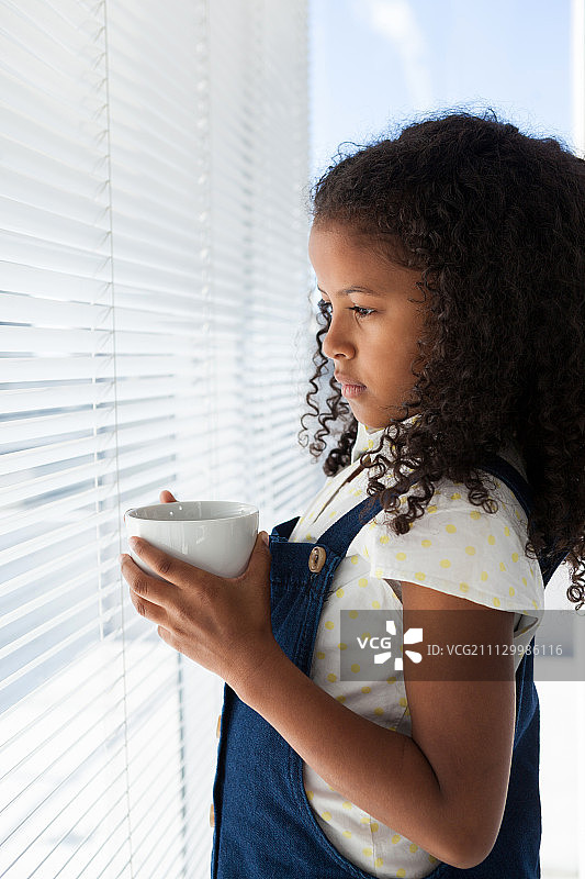 沉思的女商人站在窗边，手 holding咖啡杯的侧面视角图片素材