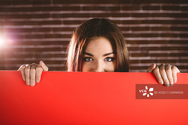 在砖墙前用白纸遮住脸的微笑女人肖像图片素材