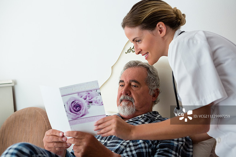 女医生向疗养院床上休息的病人展示慰问卡图片素材
