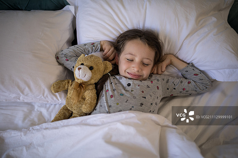 在家中卧室里抱着泰迪熊在床上睡觉的女孩图片素材