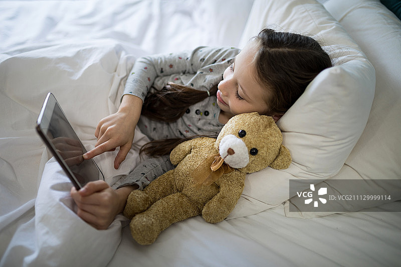 女孩在卧室的床上使用平板电脑图片素材