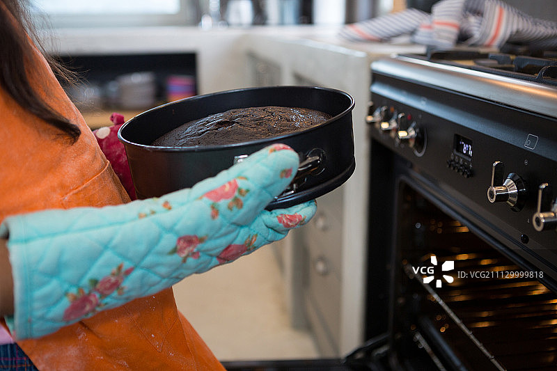 女孩拿着装有蛋糕的容器站在厨房烤箱旁的局部照片图片素材