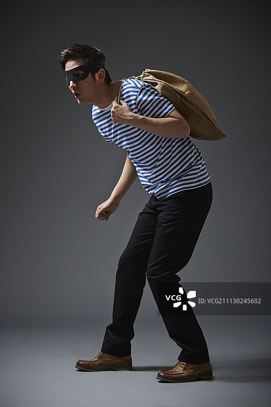 戴黑面具穿休闲装的男人肩扛麻袋图片素材