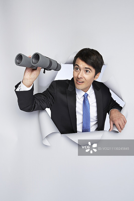 身穿西装的男子在白色背景前拿着双筒望远镜的影棚照图片素材