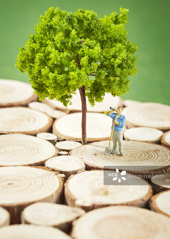 小人在树前木块上喝啤酒，手持铲子图片素材