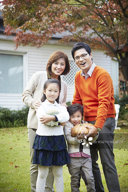 幸福的一家人在花园里，父母和孩子，男孩拿着南瓜的照片图片素材