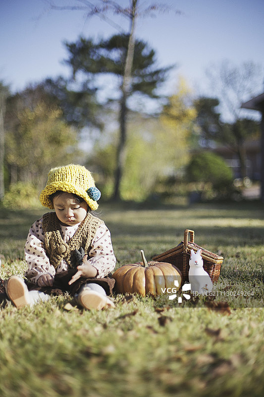 坐在草地上，野餐篮、南瓜和兔子玩具旁的女婴摄影图片素材
