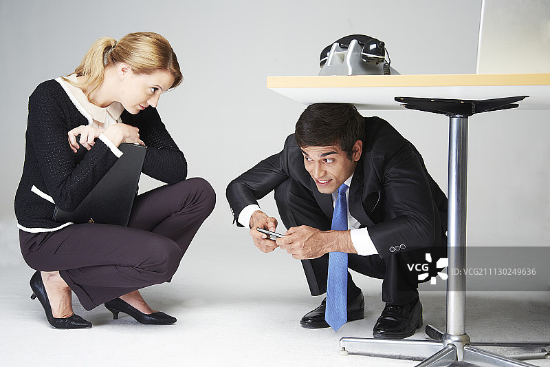 商人桌下玩手机，女商人看着他图片素材