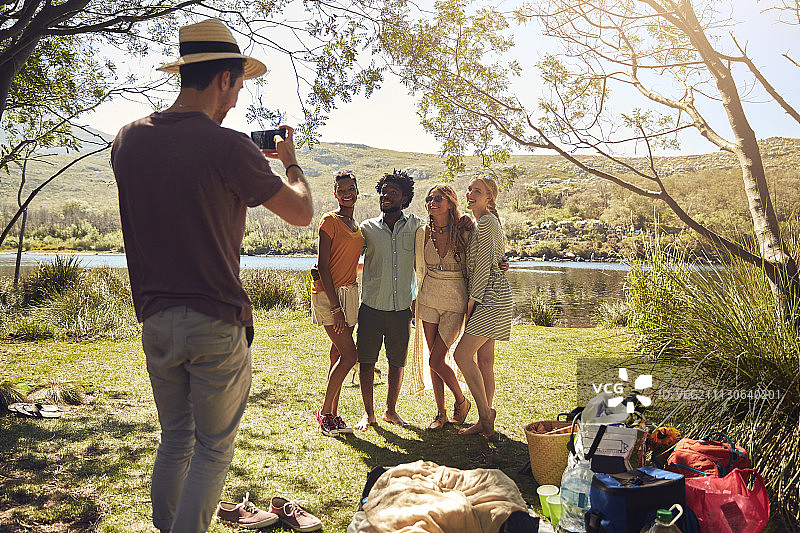 青年在阳光明媚的夏日河边给朋友们拍照图片素材