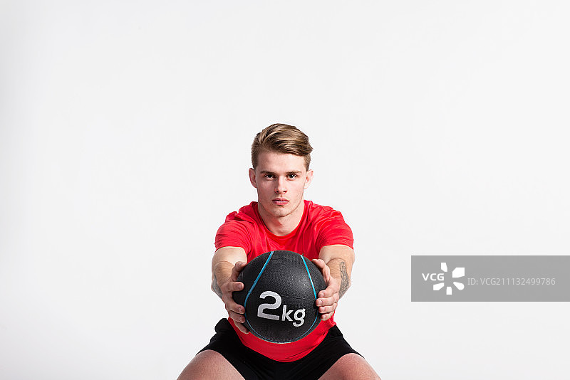 健身男人手拿药球深蹲，影棚拍摄。图片素材