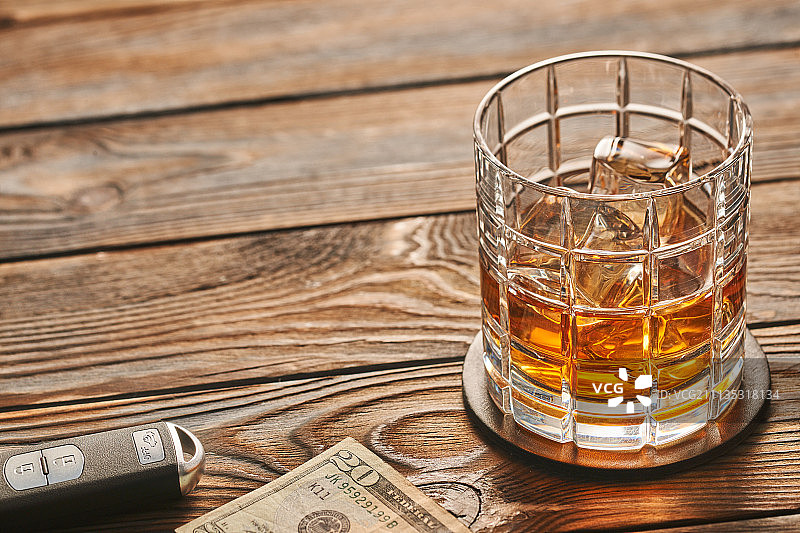 乡村木桌上放一杯威士忌或酒精饮料，带冰块和车钥匙，有复制空间。酒后驾车和酗酒概念。安全驾驶概念图片素材