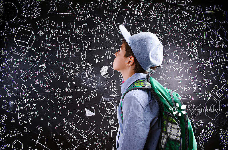 男孩背着书包，靠在有数学符号的大黑板上图片素材