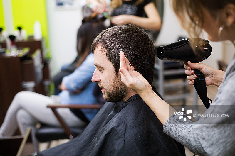 专业发型师为英俊的顾客吹干头发图片素材