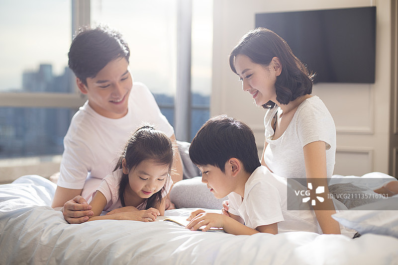 快乐的年轻家庭在床上看书图片素材