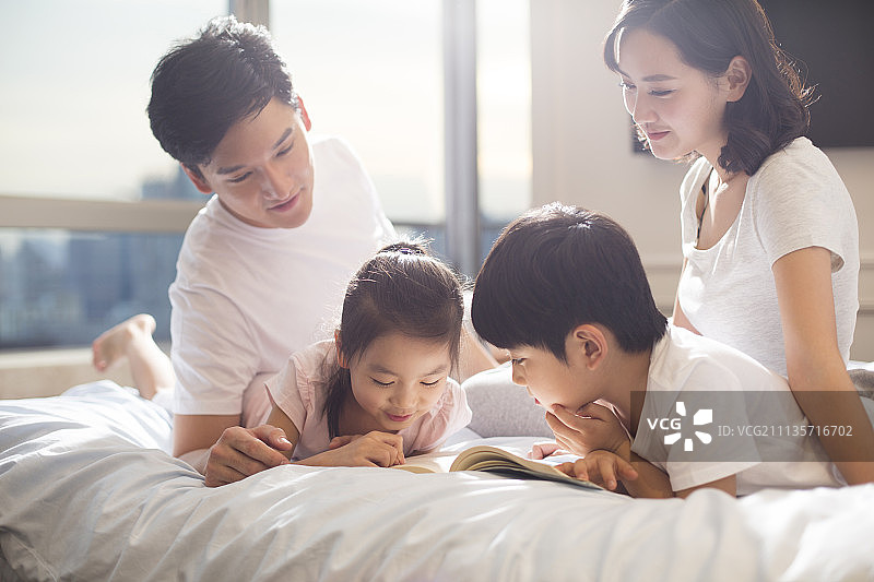 快乐的年轻家庭在床上看书图片素材