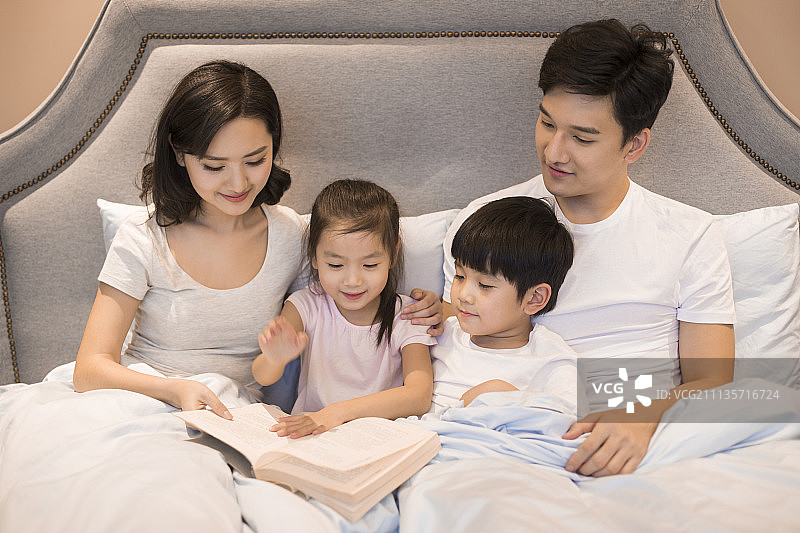 快乐的年轻家庭在床上看书图片素材