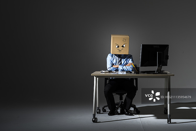 西装革履的愤怒商人，头上顶着盒子，在黑暗阴影背景下叉着双臂图片素材