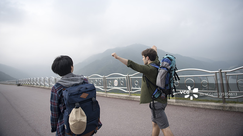 两名背包客在春川市昭阳湖和山脉的道路上行走图片素材