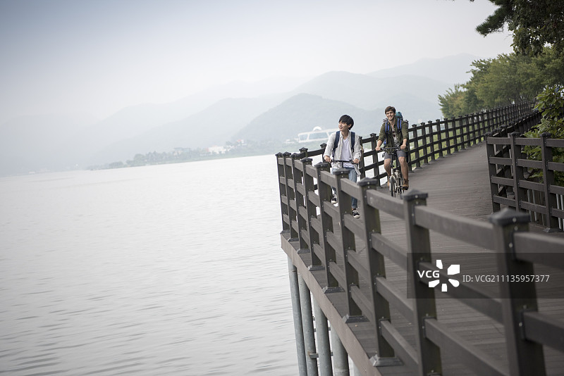 两名男子在昭阳湖沿岸的木桥上骑自行车图片素材