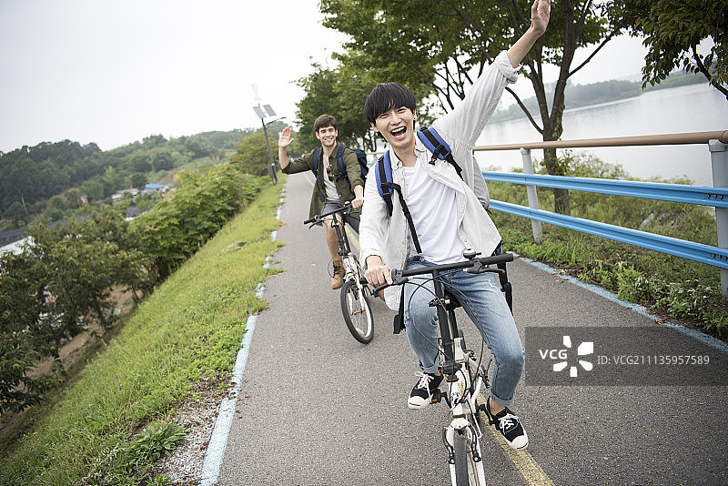 快乐的男人骑自行车，在春川市的道路上挥手图片素材