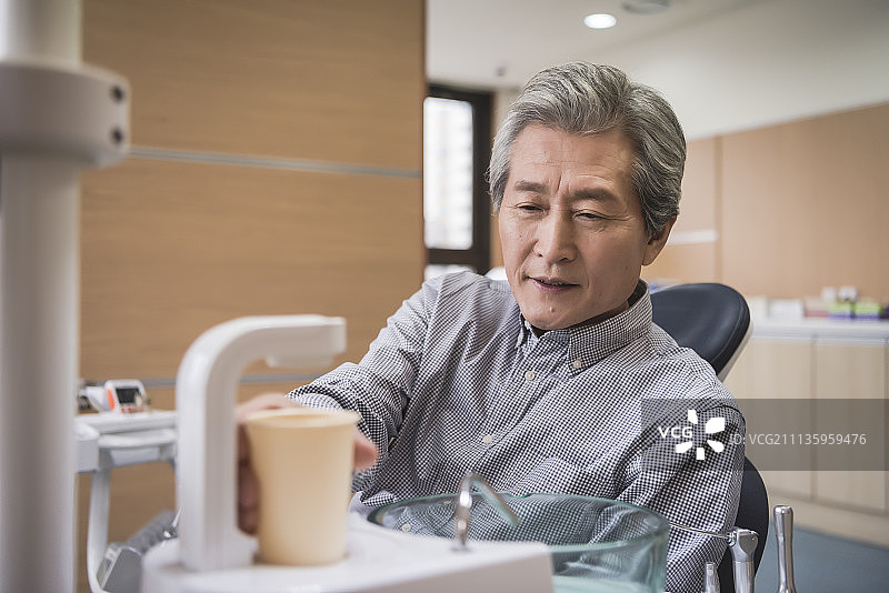 老年患者坐在牙科椅上拿着一杯水图片素材
