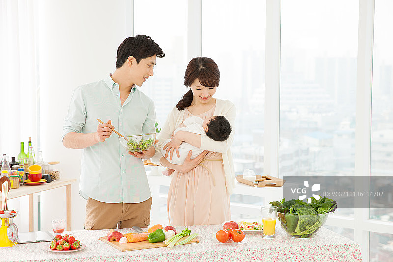 夫妇在厨房做饭，抱着婴儿，双职工家庭图片素材