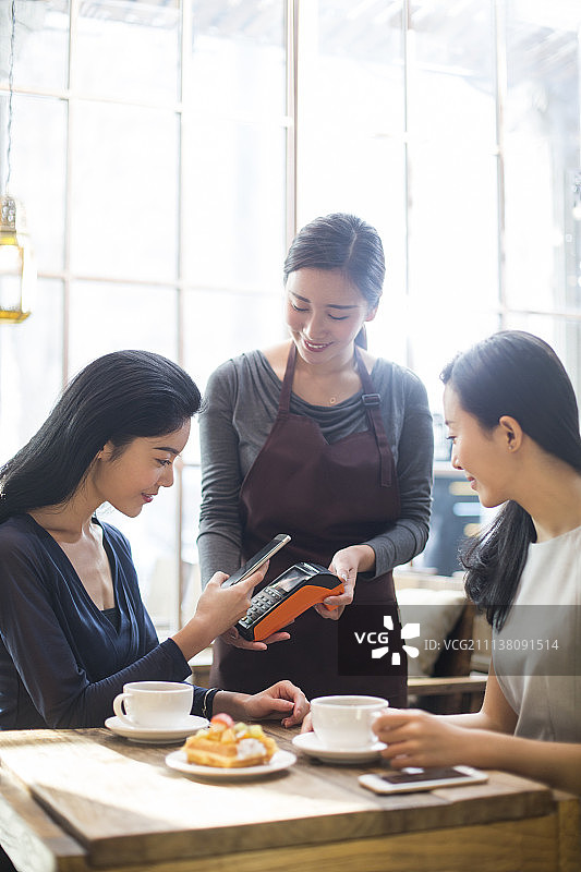 闺蜜俩在咖啡馆用手机结账图片素材
