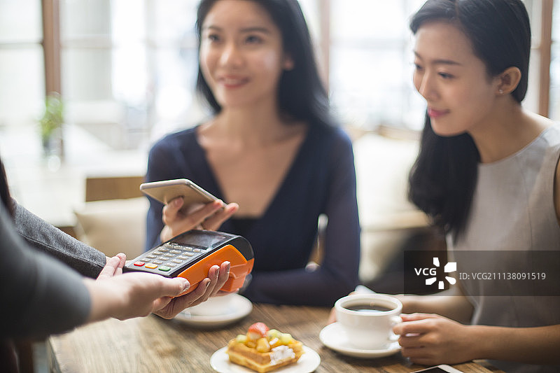 闺蜜俩在咖啡馆用手机结账图片素材