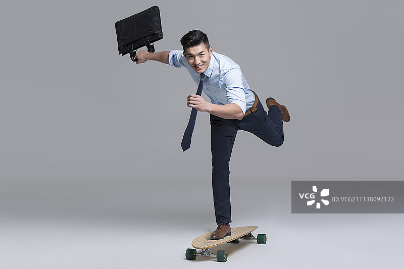 快乐的年轻商务男子拎着公文包滑滑板图片素材