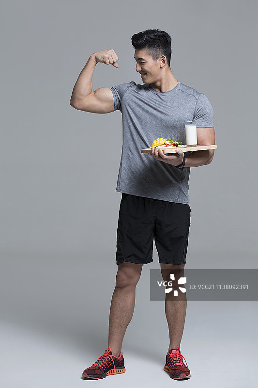 手端蔬菜沙拉和牛奶的男运动员鼓起肌肉图片素材