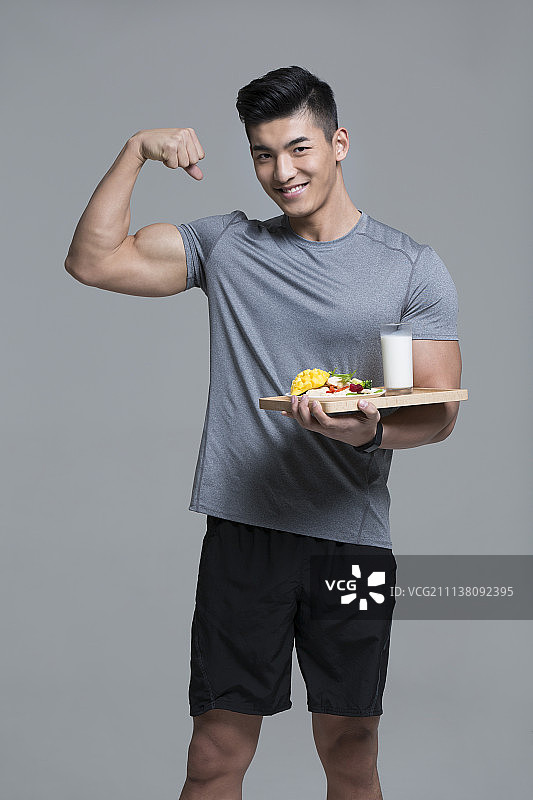 手端蔬菜沙拉和牛奶的男运动员鼓起肌肉图片素材